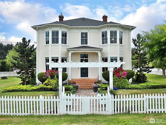 The 1894 John Gould Italianate Victorian, photographed straight-on, white clapboard facade with bay windows, central portico, and picket fence in summer light